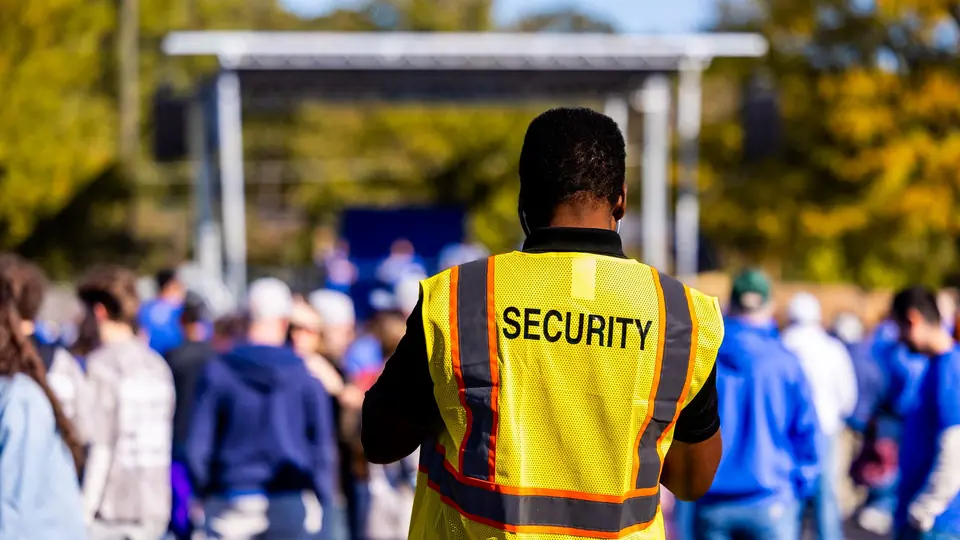 A security officer in a high-visibility vest watching over a crowd at an outdoor event
