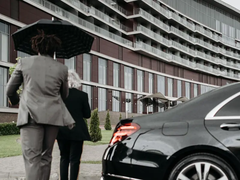 A man in a dark suit standing beside a car